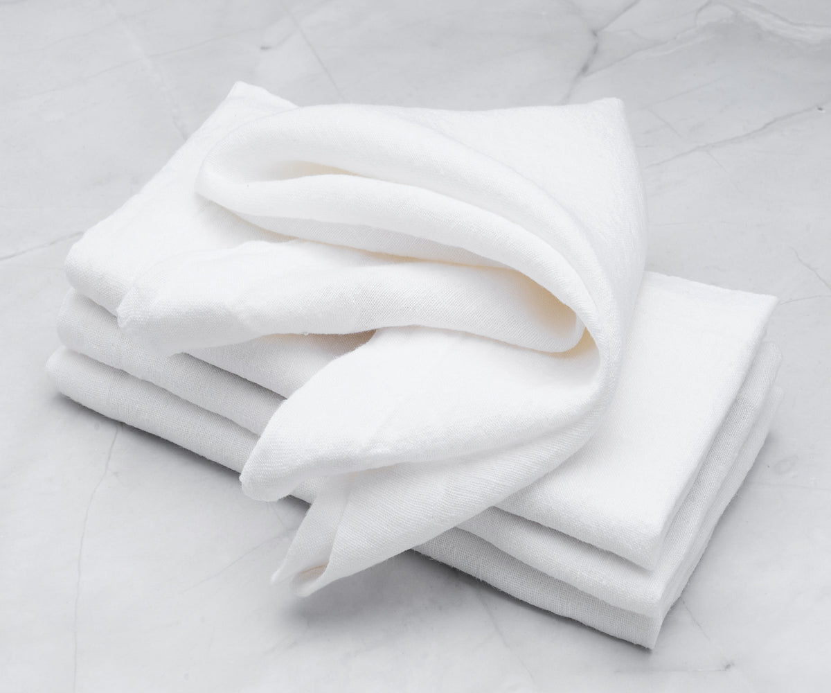 Multiple white dinner napkins stacked on a marble countertop