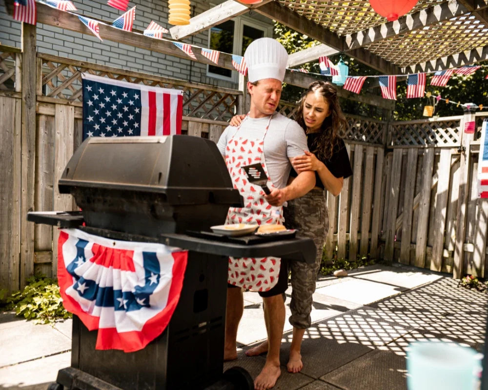 Couple grilling together during a festive 4th of July BBQ with American flag decorations and summer backyard setup.