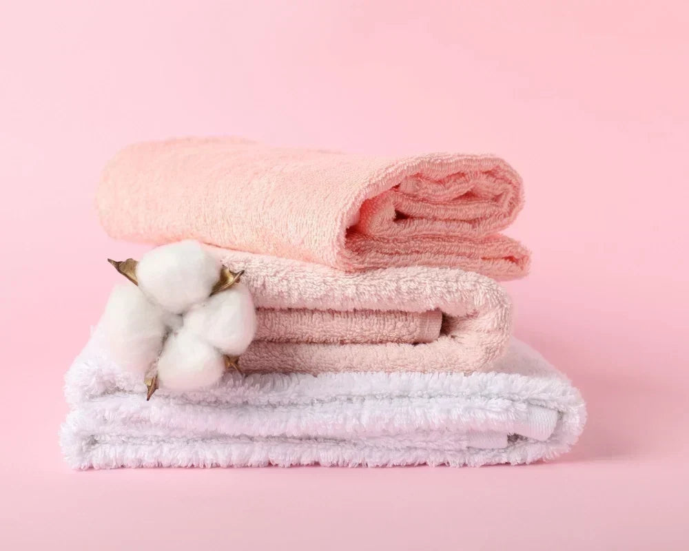 White cotton bath towels and bath sheets neatly folded and stacked in a bright bathroom setting