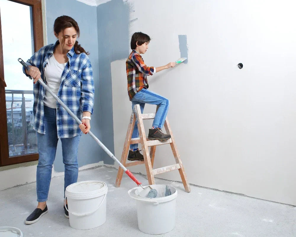 Woman and child painting a bedroom together, using buckets and a ladder.