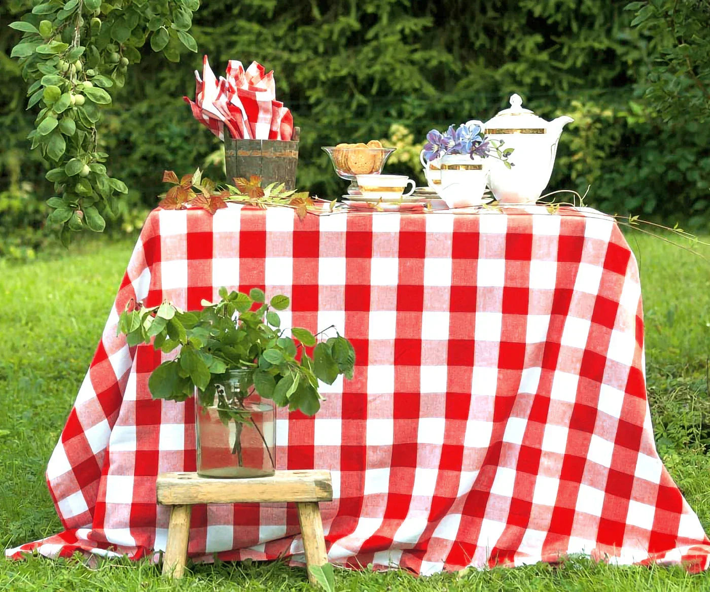 Outdoor picnic table covered with a classic red and white buffalo plaid tablecloth in a lush garden setting.