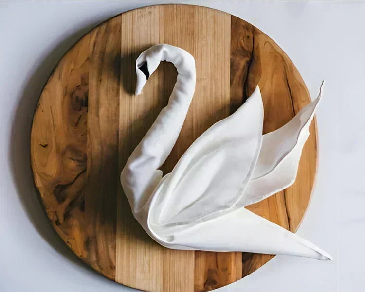 Linen napkin folded into a swan on a round wooden board
