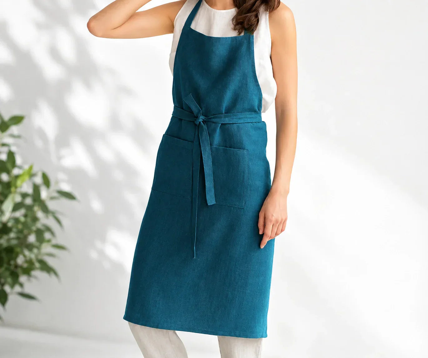 Woman wearing a teal linen apron in a bright studio.