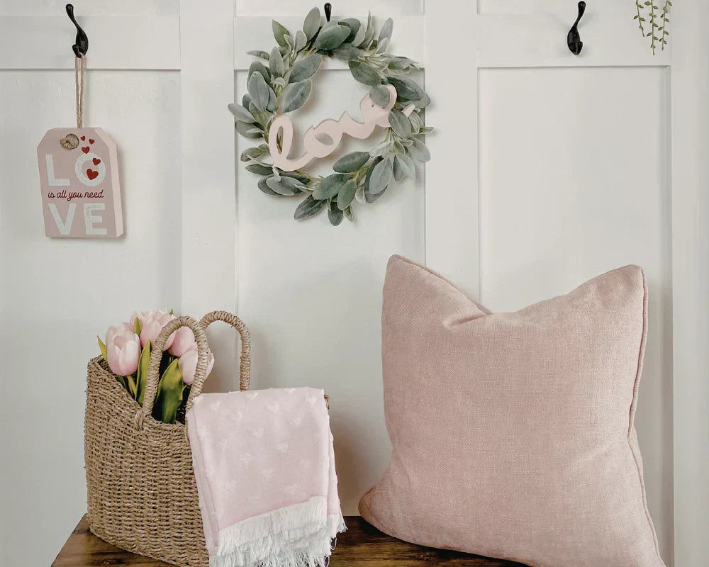 Decorative elements including a pink pillow, basket with flowers, and wreath on a white wall.