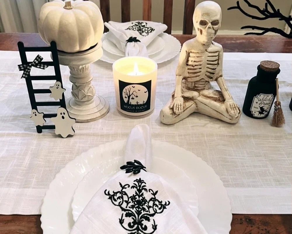  White Halloween table decor with pumpkins, skeleton, ghost accents, candles, and floral napkins on a dining table.