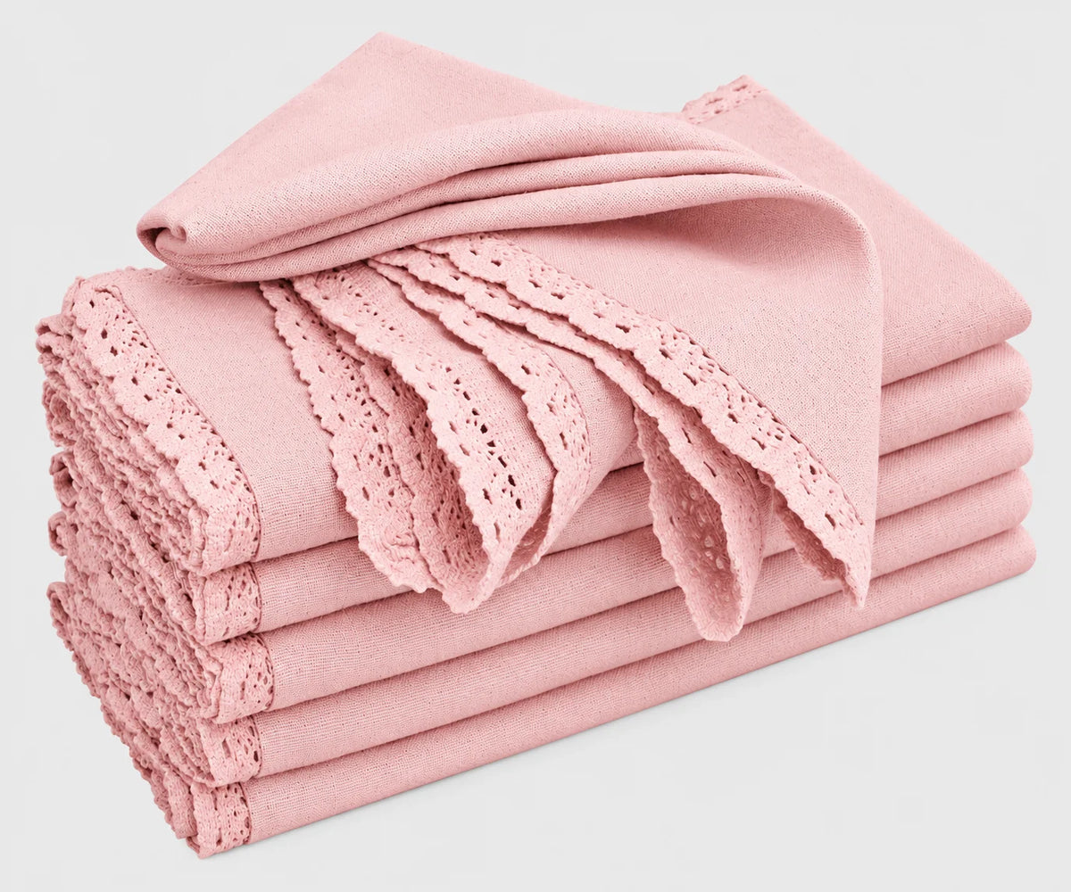 A stack of folded baby pink cotton cloth napkins featuring delicate lace trim and cutwork edges