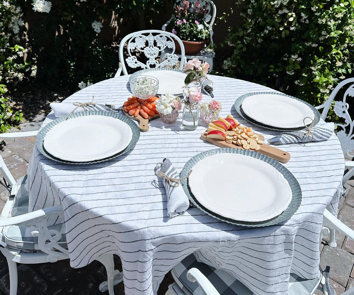 Elegant dining setup with a round linen tablecloth, white plates, and silver cutlery.