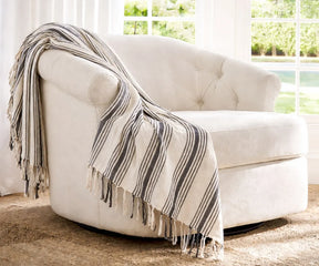 Lightweight cotton throw blanket draped over a comfortable chair in a bright and airy living room