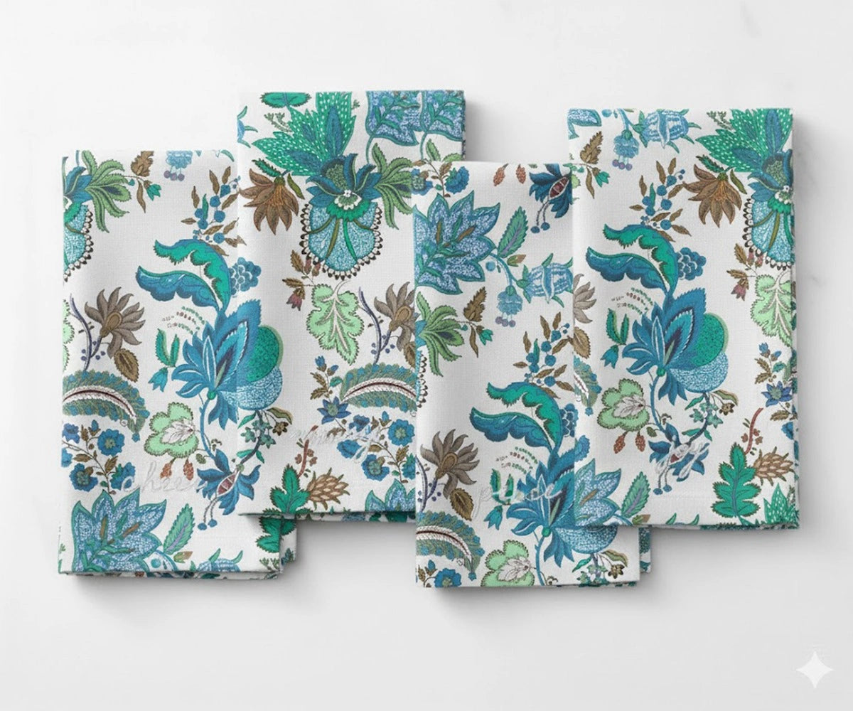 Elegant cotton napkin with a detailed blue and green botanical design, showcasing floral and leafy motifs in teal, aqua, and earthy tones on a white base.