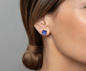 Woman wearing a gold stud earring with a square-cut deep blue gemstone.