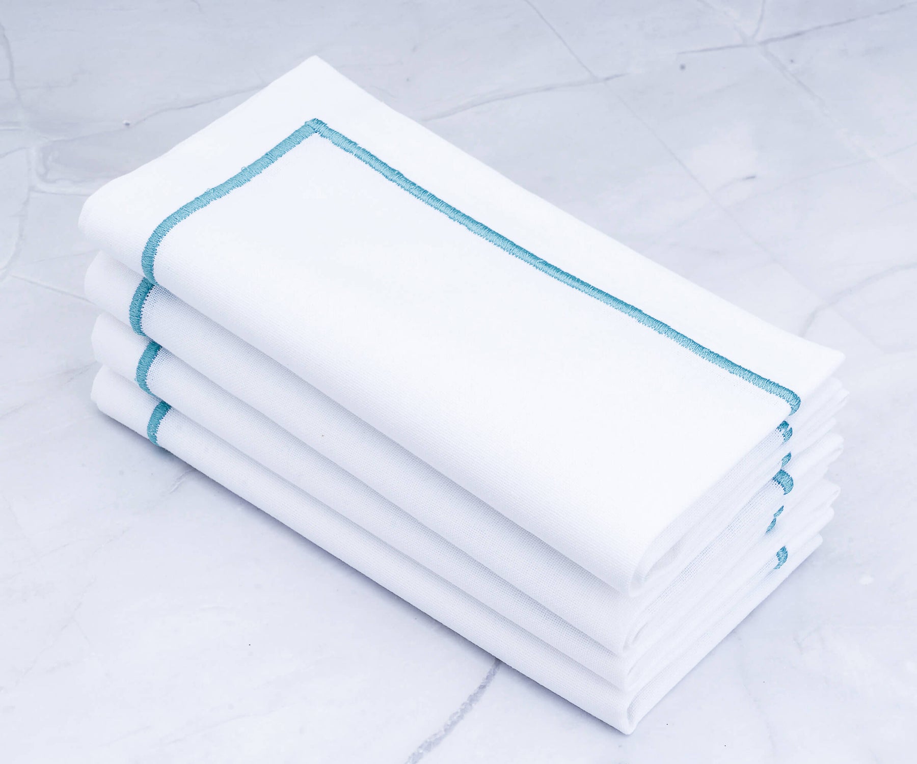 Set of four white dinner napkins with blue trim on a marble countertop