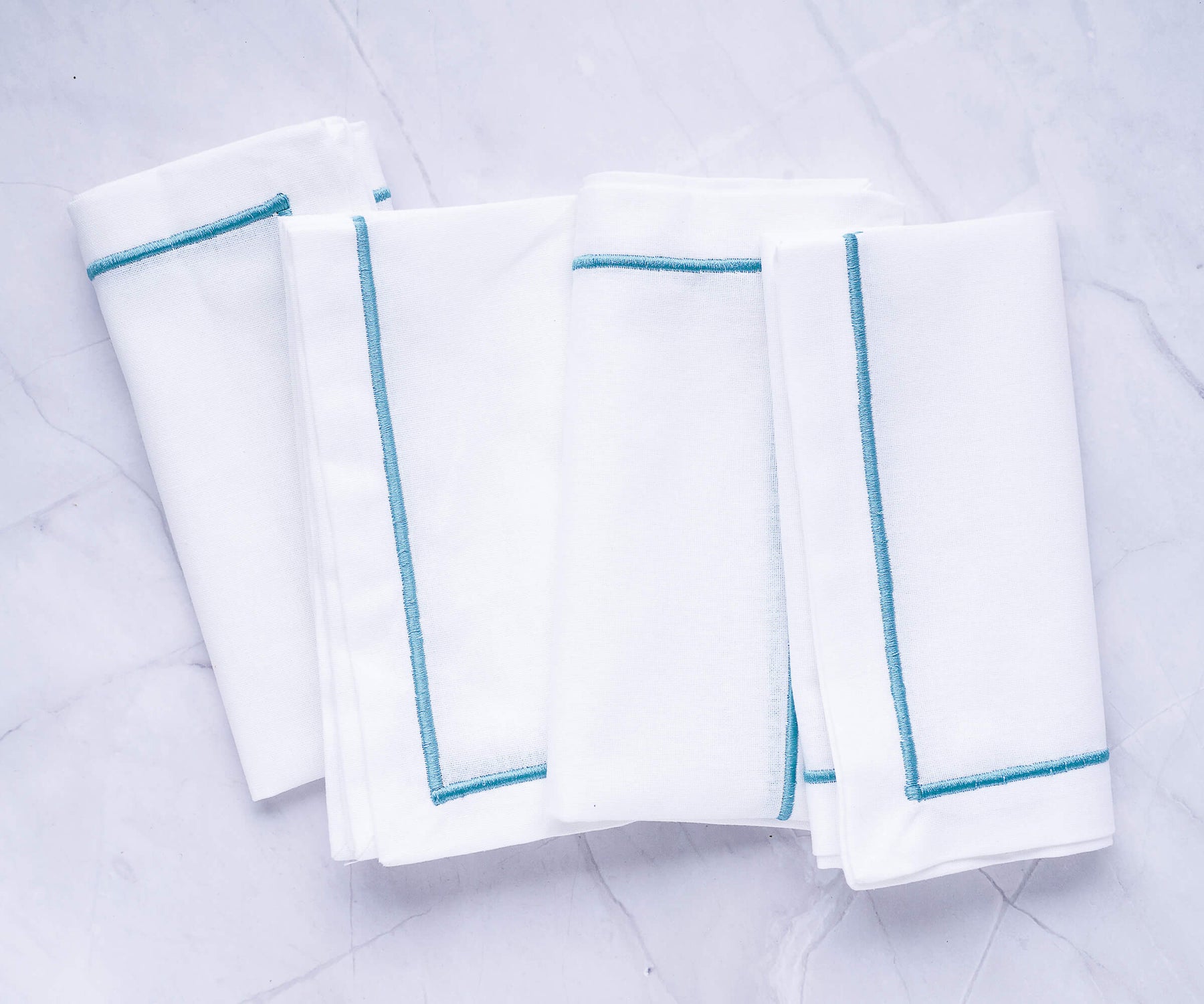 Four white dinner napkins with blue trim displayed together