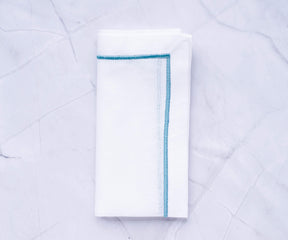 White dinner napkin with blue trim displayed on a marble surface