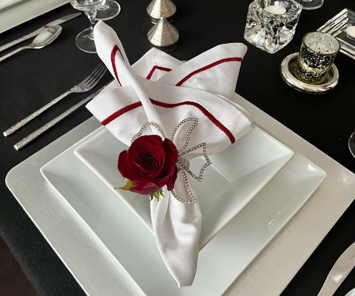 Place setting with a red rose and a white dinner napkin on a plate