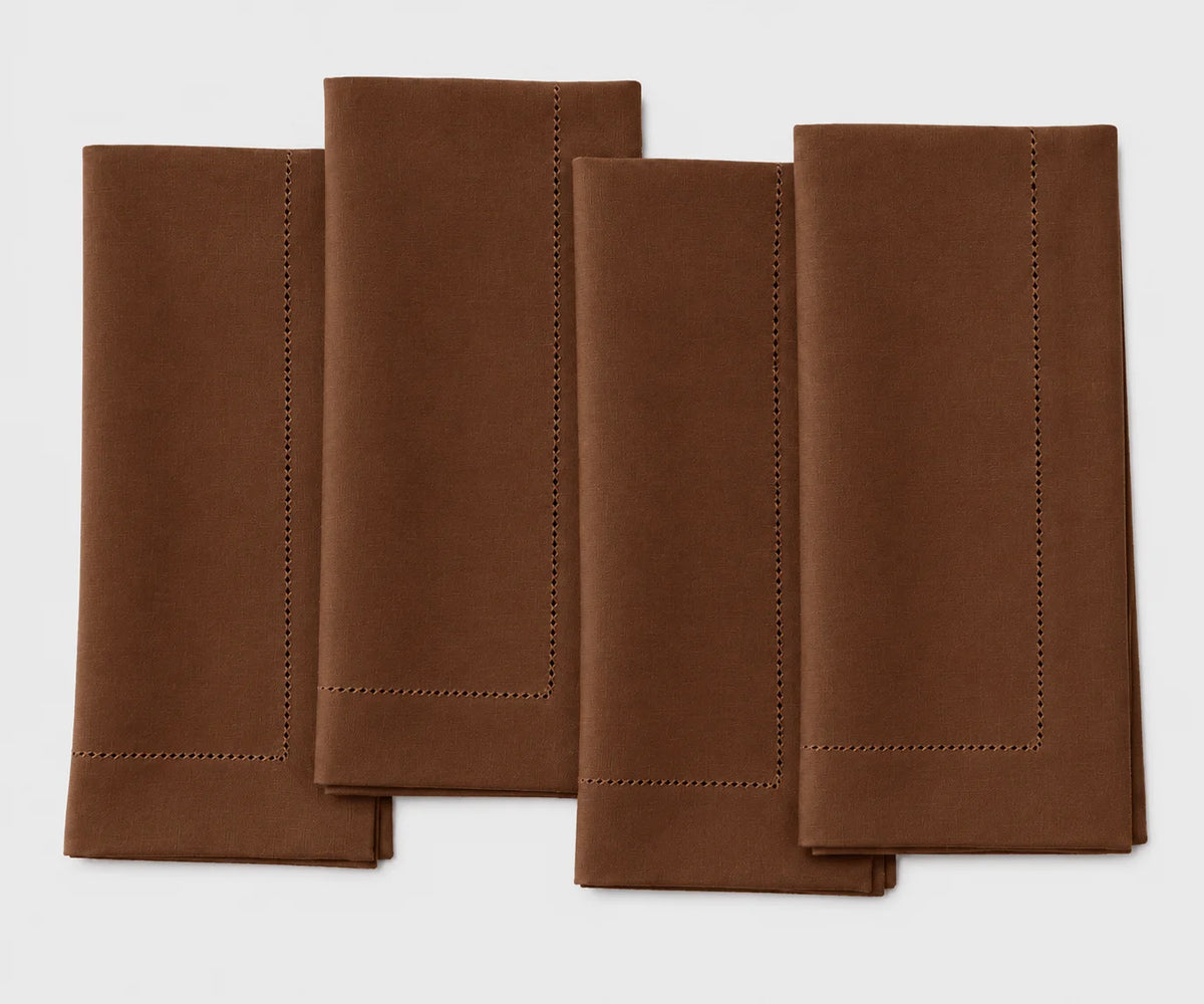 Four folded brown napkins with stitched borders arranged in a staggered stack on a white background.