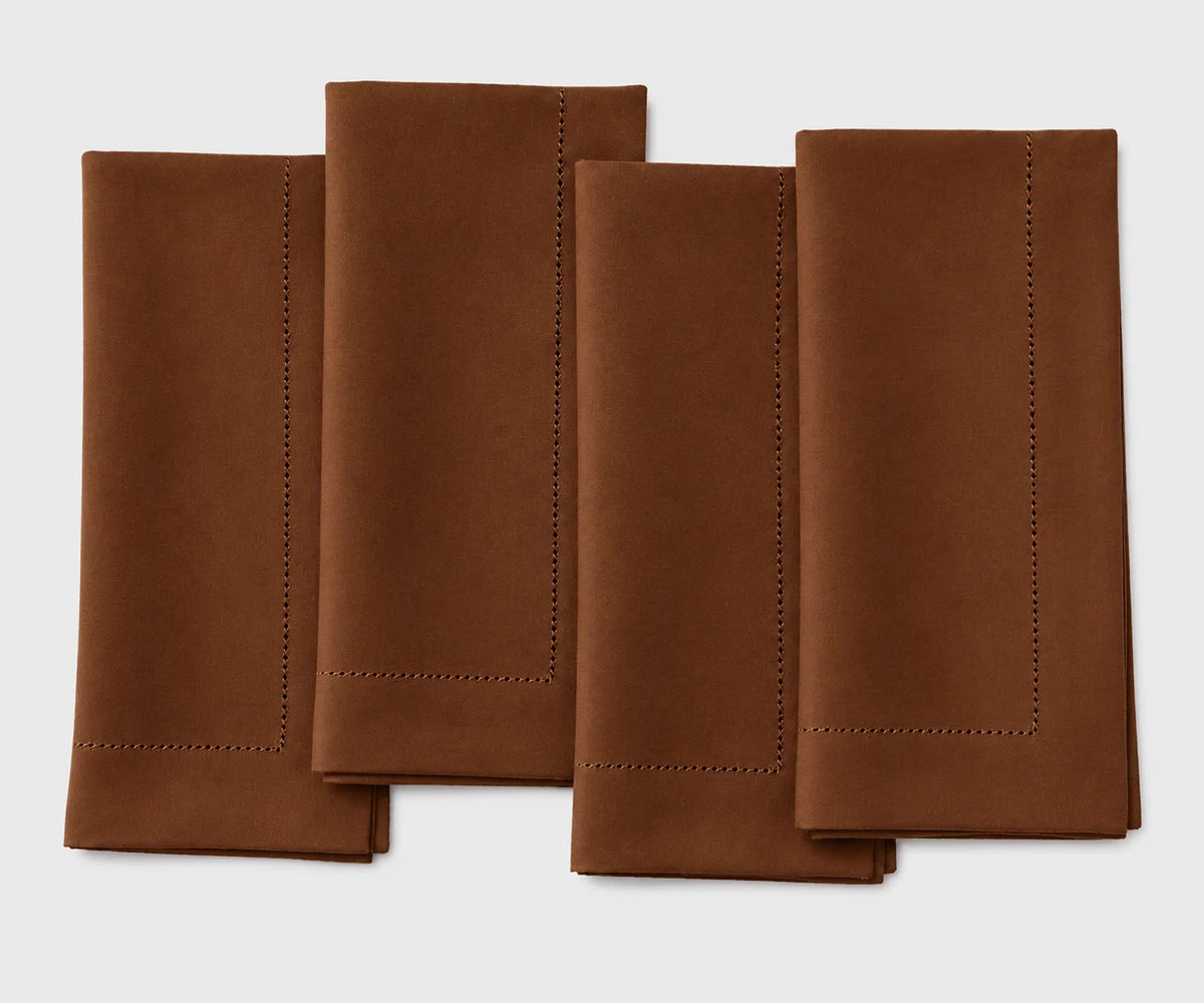 Set of four coffee brown hemstitch dinner napkins neatly folded side by side on a white background