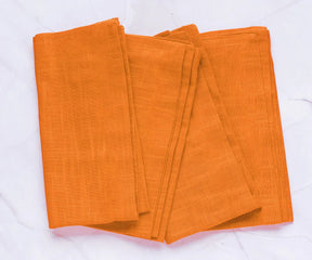 Set of 12 Clementine Orange cotton napkins neatly folded on a summer table, made from 100% cotton – perfect for vibrant seasonal dining.