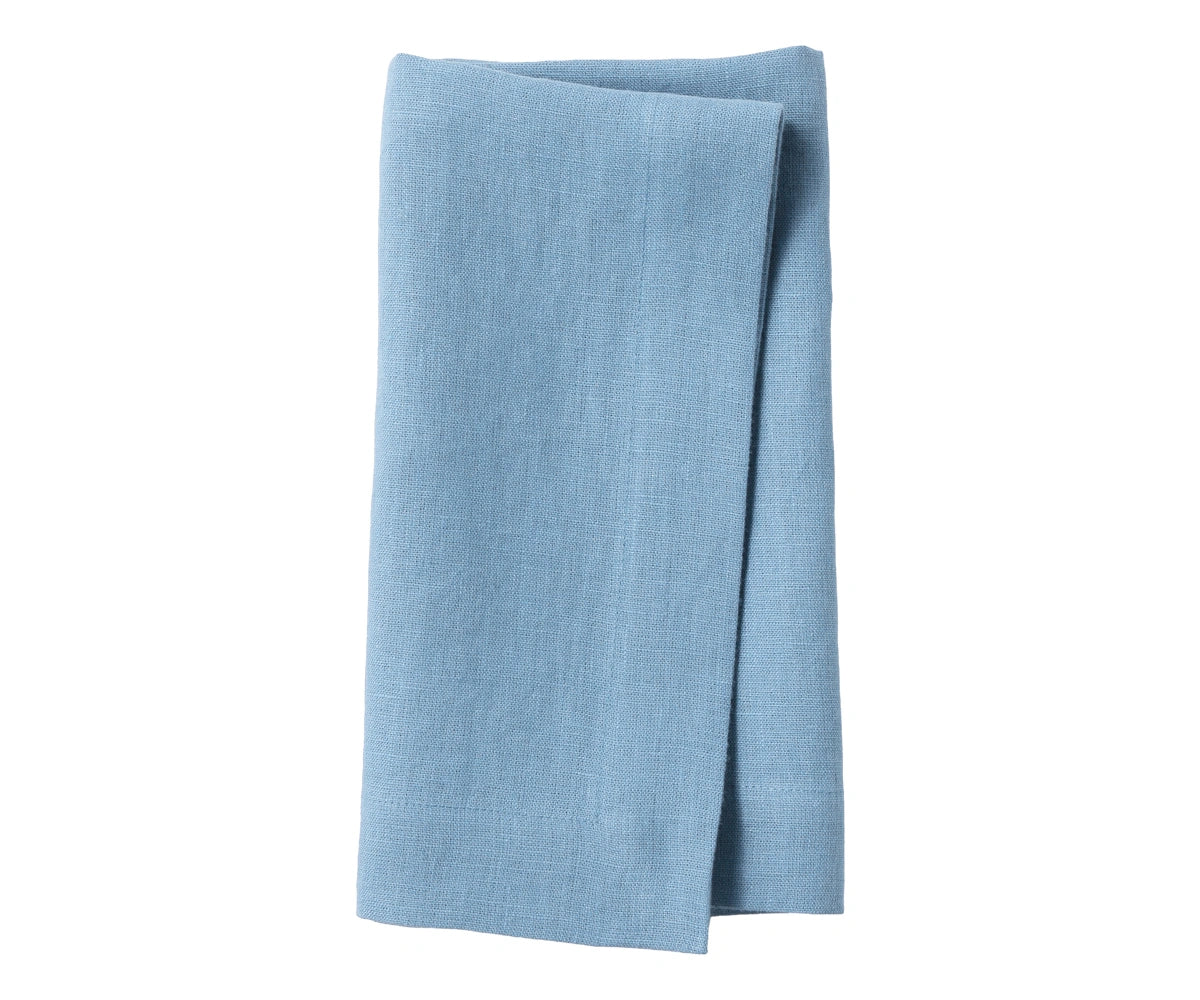 Cornflower blue plain linen napkin arranged on dining table, showing soft textured fabric