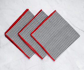 Rolled black striped napkin with red trim placed on a dinner plate for an elegant look.