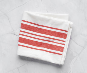 A set of kitchen towels with orange and white stripes displayed on a marble countertop