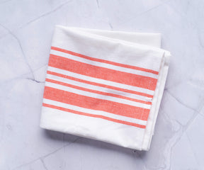 A set of kitchen towels with orange and white stripes displayed on a marble countertop