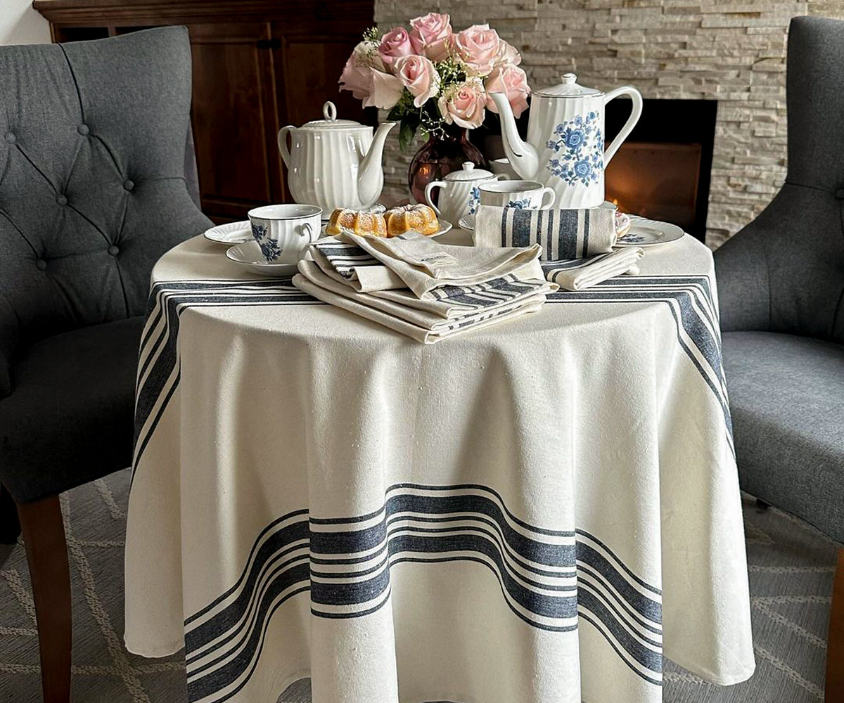 An elegant dining room tablecloth adorned with intricate patterns, neatly draped over a wooden dining table set with fine china and crystal glassware, creating a sophisticated and inviting ambiance.