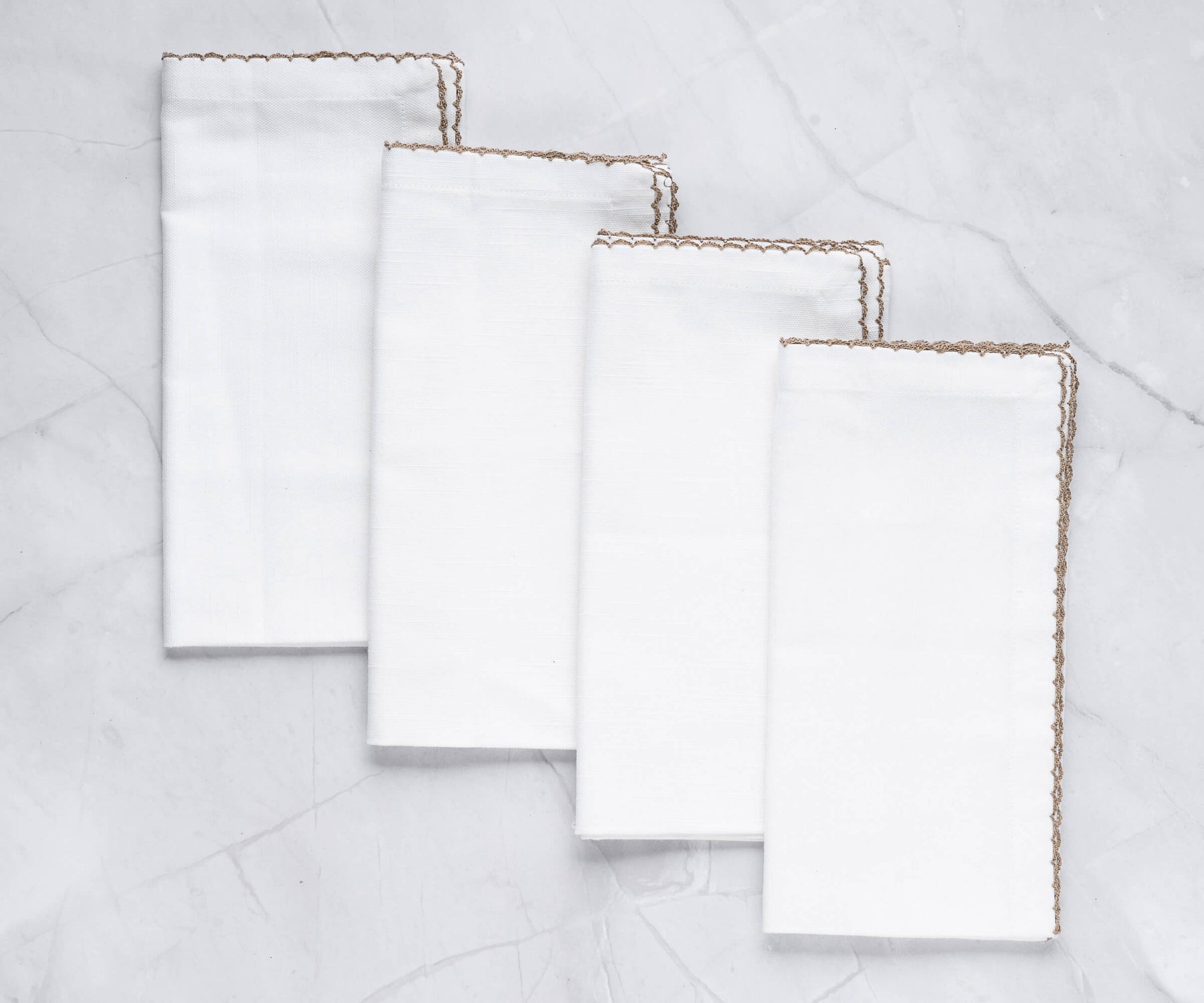 Four luxurious shell edge napkins with gold trim arranged on a marble countertop