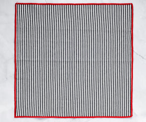black cotton napkin showcasing red border stitching and fine texture.