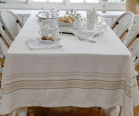Dining room table with a French tablecloth in red and white stripes and white chairs.