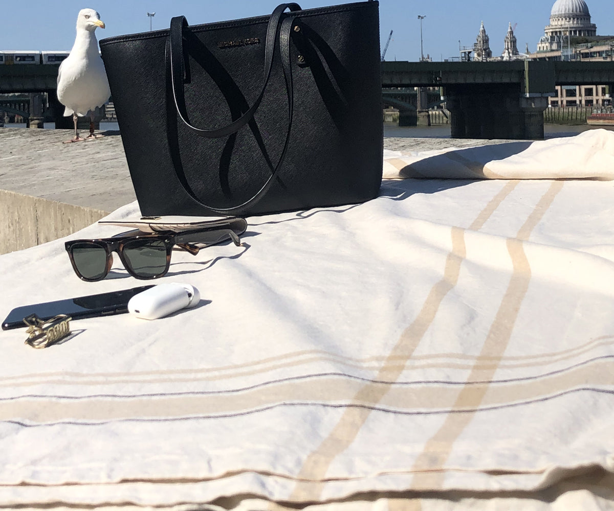 Accessories placed on a French tablecloth: a black purse, sunglasses, and a cell phone