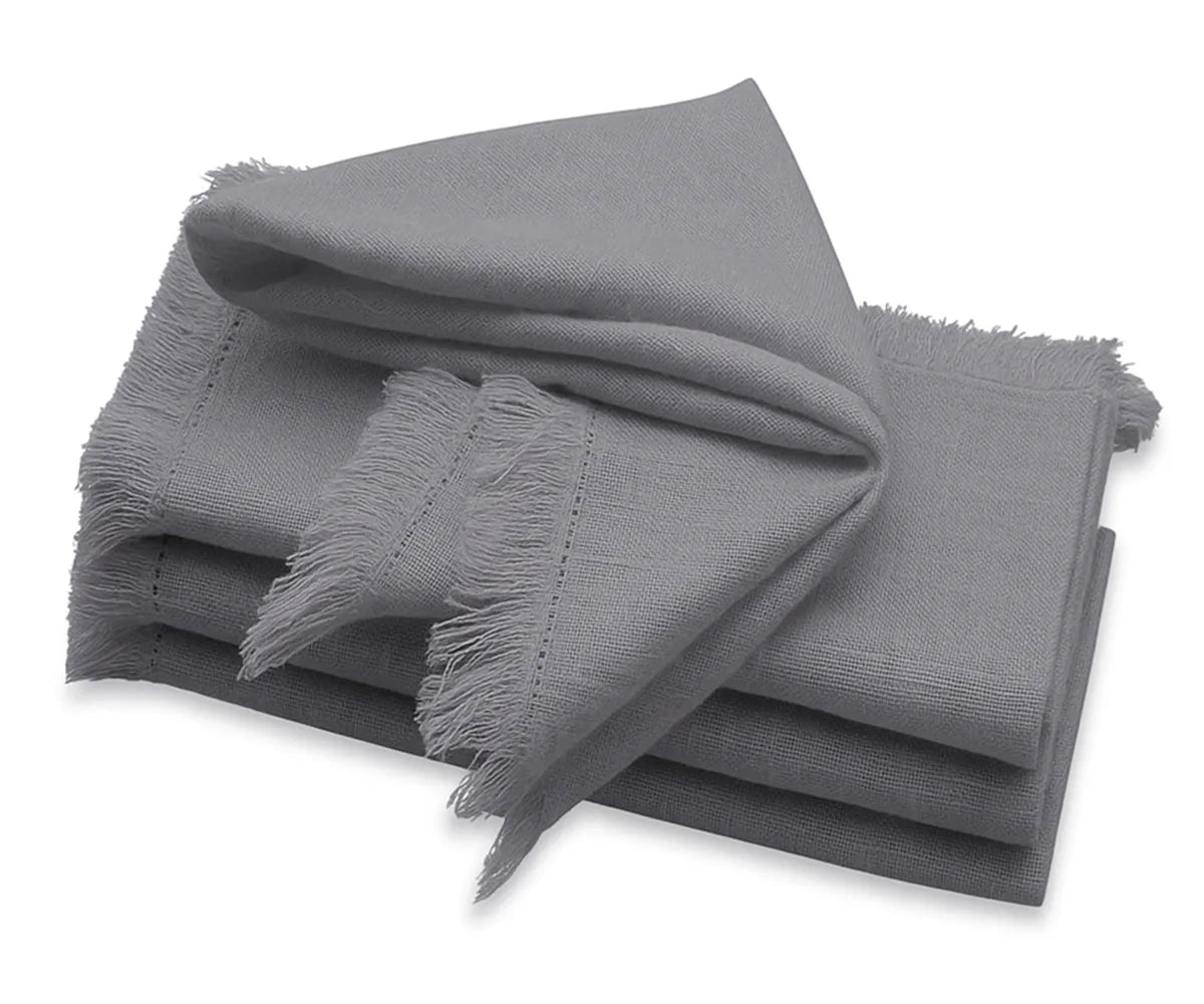 Grey fringe cotton napkins with frayed edges neatly folded on a dining table.