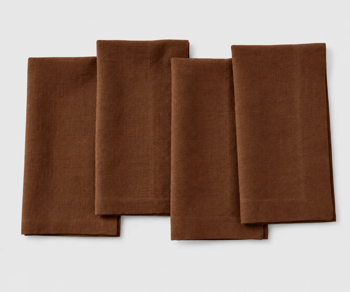 Set of four coffee brown signature linen napkins neatly folded side by side on a white background