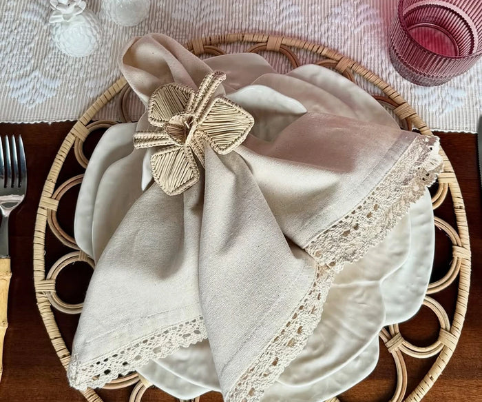 Decorative napkin with a gold butterfly clip on a woven plate with cutlery.