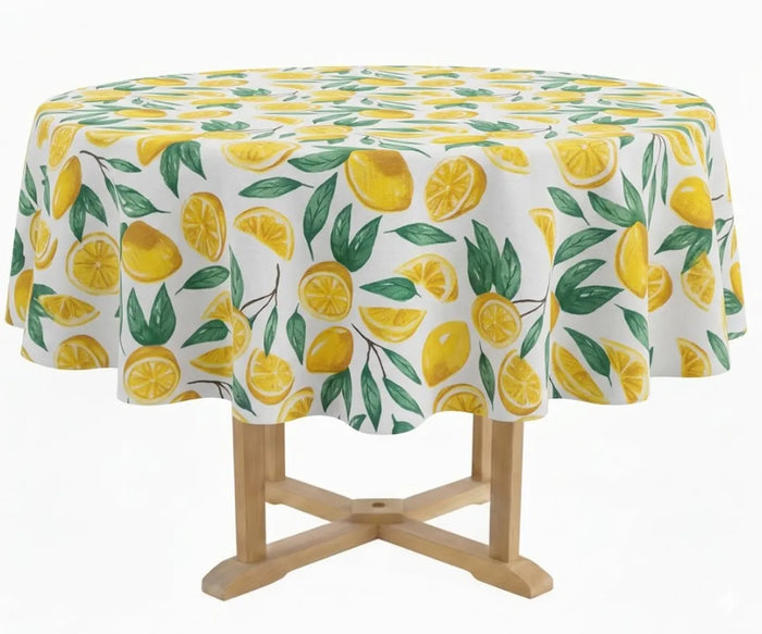 60-inch round cotton tablecloth with yellow lemon and green leaf print on white background, styled on an outdoor garden dining table with ceramic plates and rattan accents