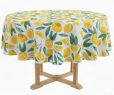 60-inch round cotton tablecloth with yellow lemon and green leaf print on white background, styled on an outdoor garden dining table with ceramic plates and rattan accents