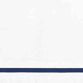 Close-up detail of white linen pillowcase with a navy blue embroidered border line.