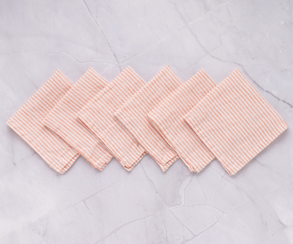 A set of six pink and white striped linen napkins displayed on a marble countertop