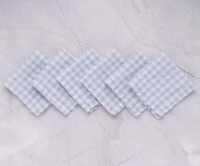Six linen napkins with blue and white gingham design on a marble surface