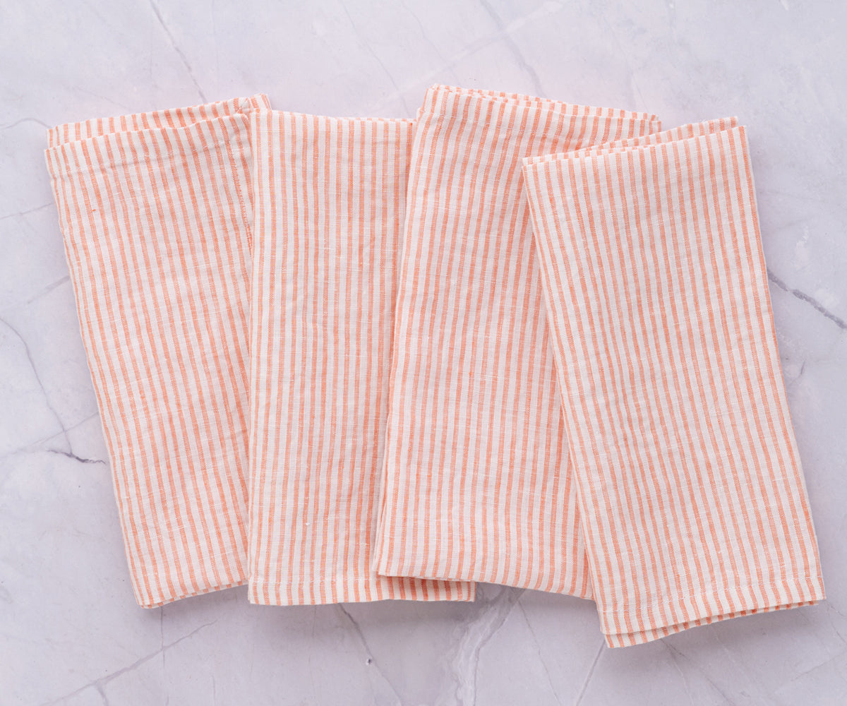 A collection of orange and white striped linen napkins arranged on a marble surface