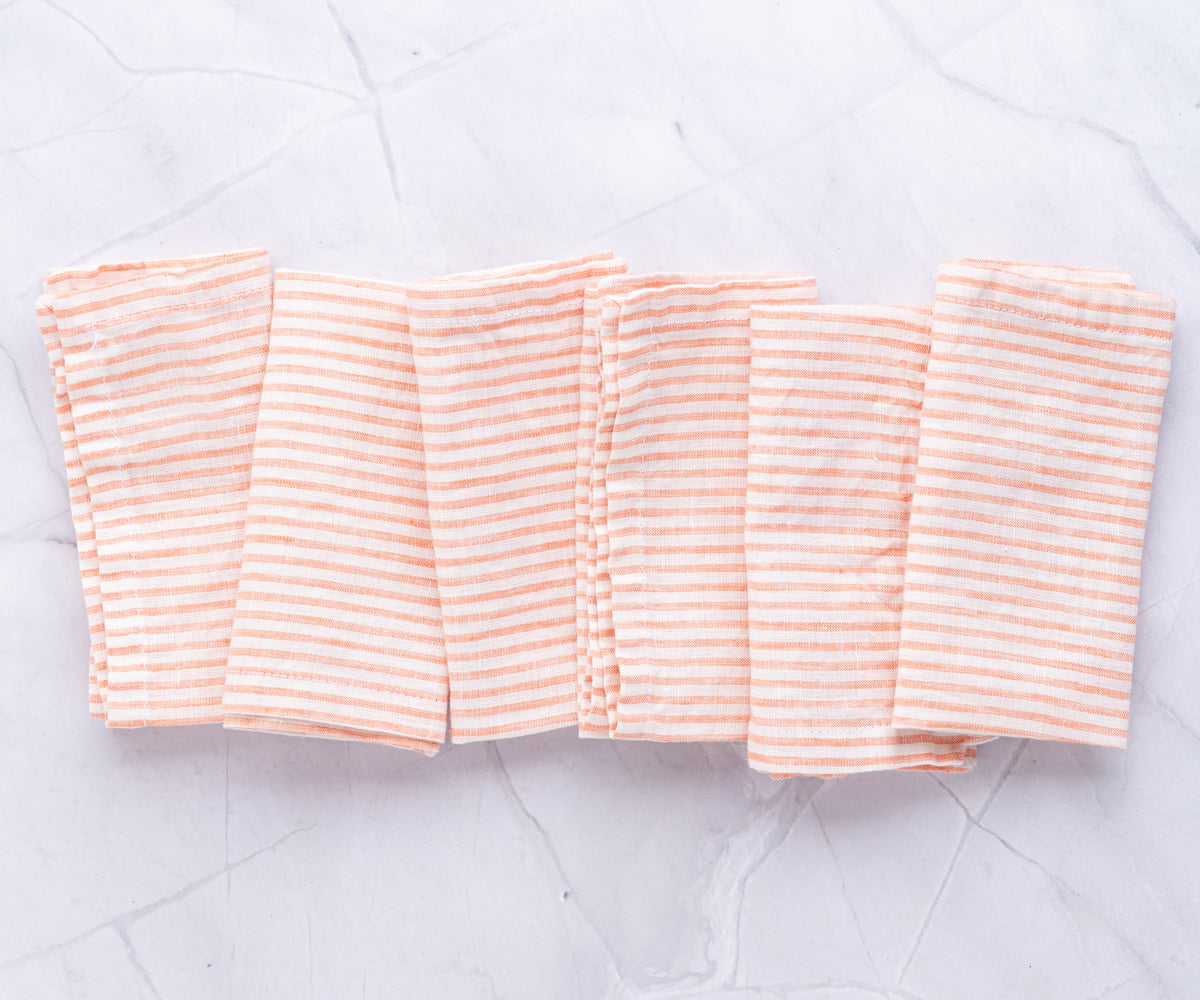 Four neatly folded orange and white striped linen napkins