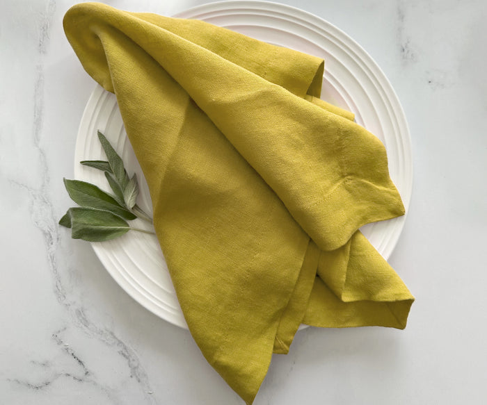 Mustard yellow linen napkin draped on a white ceramic plate with sage leaves