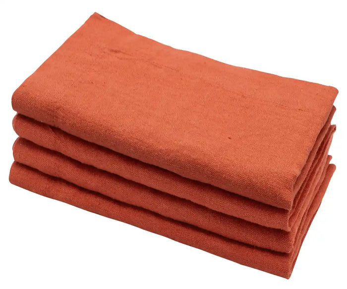 A set of four folded pink linen napkins on a marble surface with a branch of a purple flower to the side.