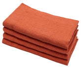 A set of four folded pink linen napkins on a marble surface with a branch of a purple flower to the side.