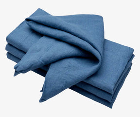 The photo features folded napkins in a shade of blue, possibly denim or a similar hue, made from a textured linen fabric.