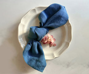A neatly stacked set of four blue linen napkins, showing their soft texture and folded edges.