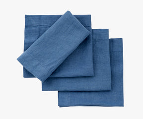 A pile of four blue fabric napkins, possibly linen, with visible weave and subtle wrinkles, indicating their natural material.