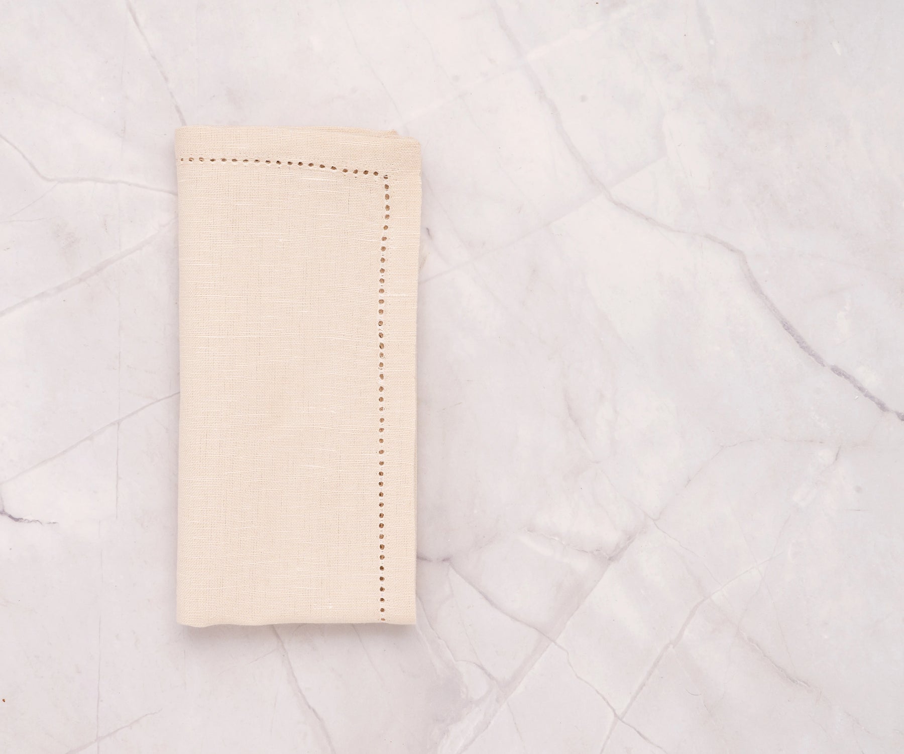 Natural hemstitch cotton linen napkins neatly folded on a dining table – soft beige napkins with elegant stitched border.