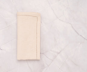 Natural hemstitch cotton linen napkins neatly folded on a dining table – soft beige napkins with elegant stitched border.