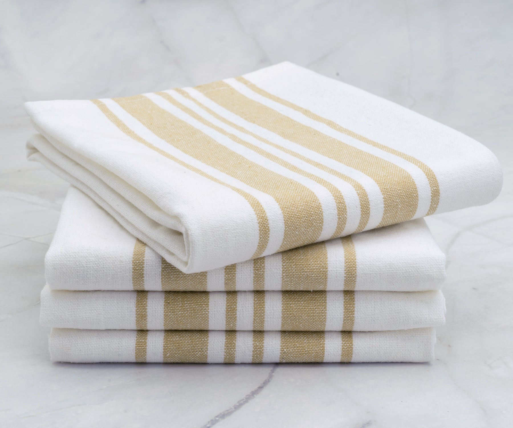 An array of white kitchen towels with gold stripes arranged on a marble surface