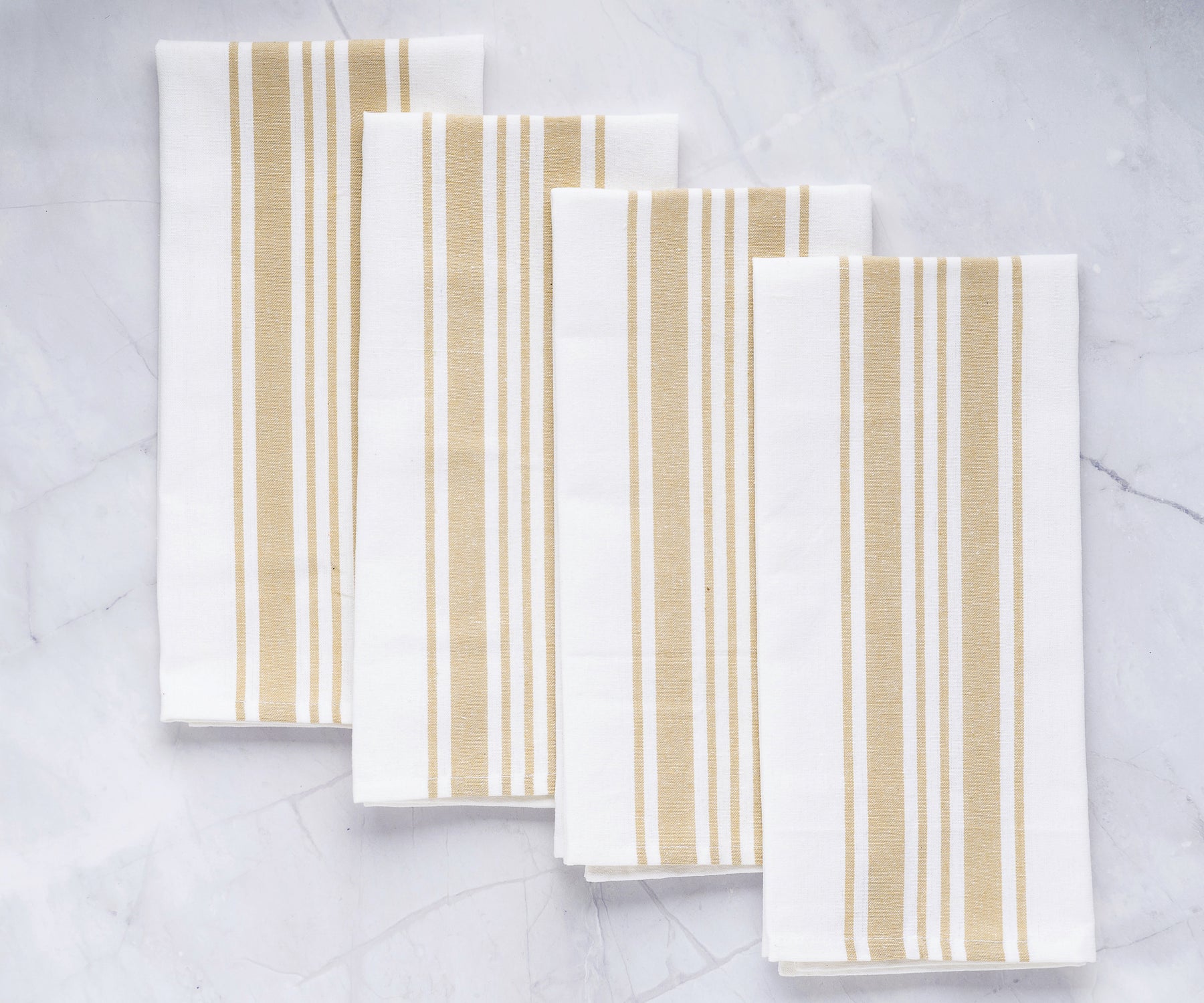 A quartet of white kitchen towels with gold stripes presented on a marble surface